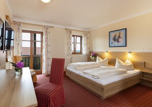 A hotel room with a bed, a desk, a chair, a TV, and a window with curtains. - Landgasthof Zum Kirchenwirt (Thyrnau)