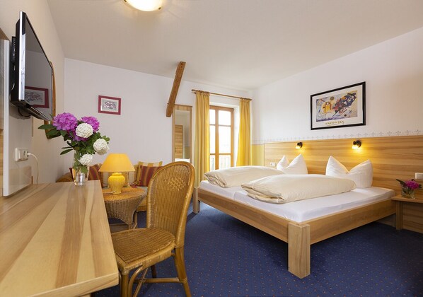 A hotel room with a wooden bed, a desk, a chair, a TV, and a window with curtains. - Landgasthof Zum Kirchenwirt (Thyrnau)