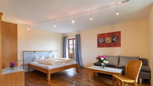 A modern room with a wooden bed, a sofa, a chair, and a small table. - Landgasthof Zum Kirchenwirt (Thyrnau)