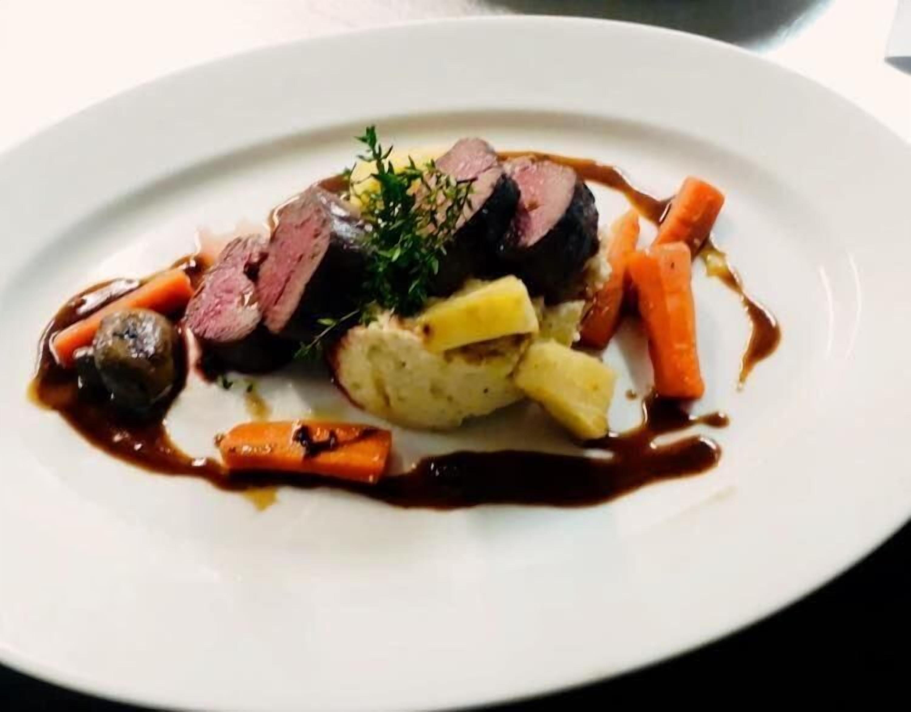 A plate of food with sliced meat, carrots, potatoes, and mushrooms.