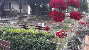 Een terras met tafels en stoelen, omringd door groen en een boom.