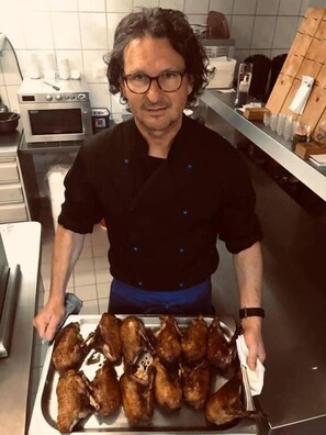 A person holding a tray of roasted chickens in a kitchen. - Landgasthof Zum Kirchenwirt (Thyrnau)