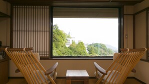 A room with two wooden chairs and a small table, a window with a view of trees and buildings, and traditional sliding doors.