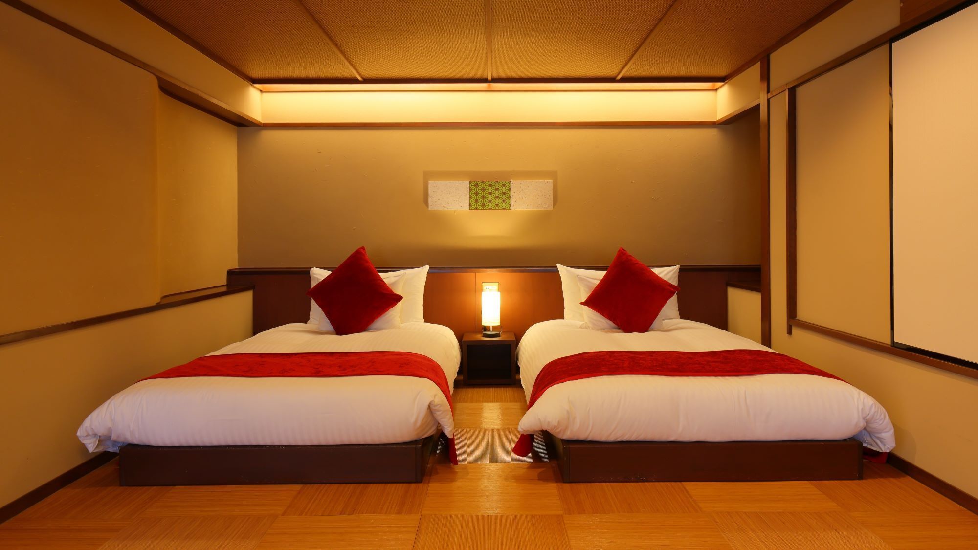 Een hotelkamer met twee bedden, een nachtkastje met een lamp en een plafondlamp.