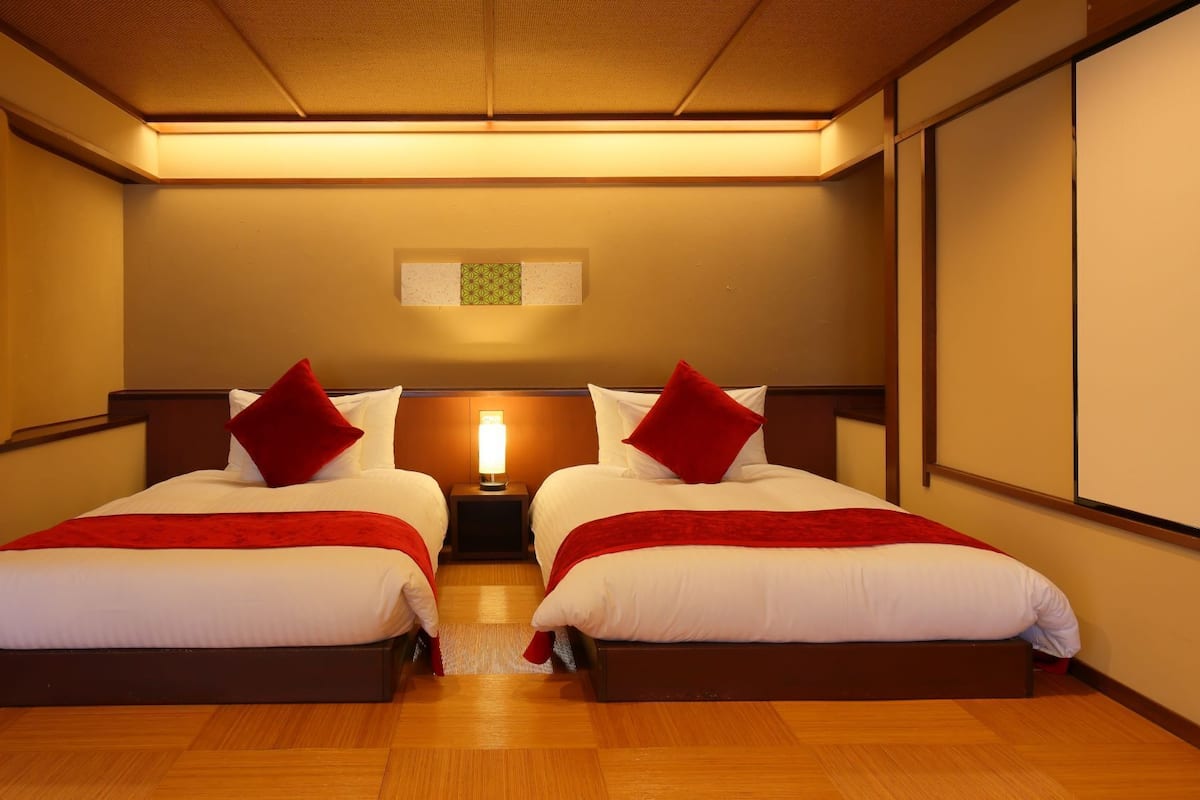 A hotel room with two beds, a nightstand with a lamp, and a ceiling light.