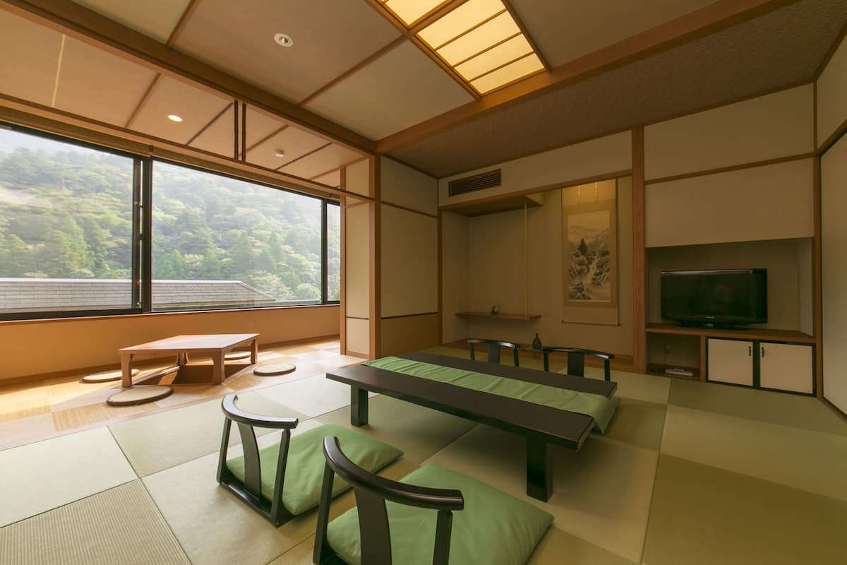 Une pièce de style japonais traditionnel, avec un sol recouvert de tatamis, une table basse, des bancs et un téléviseur.
