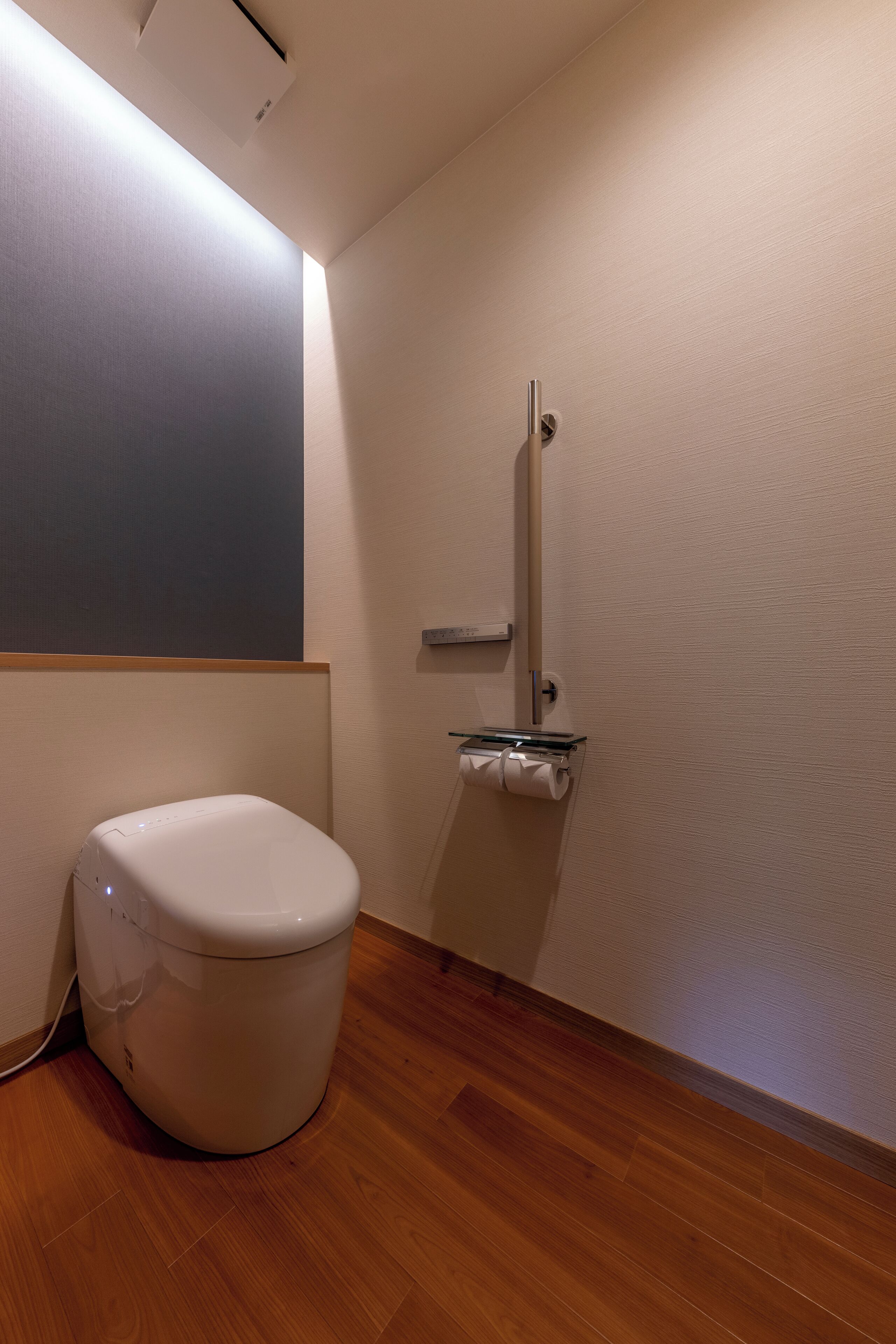 A bathroom with a toilet, a glass-encased bidet, and a wooden floor.