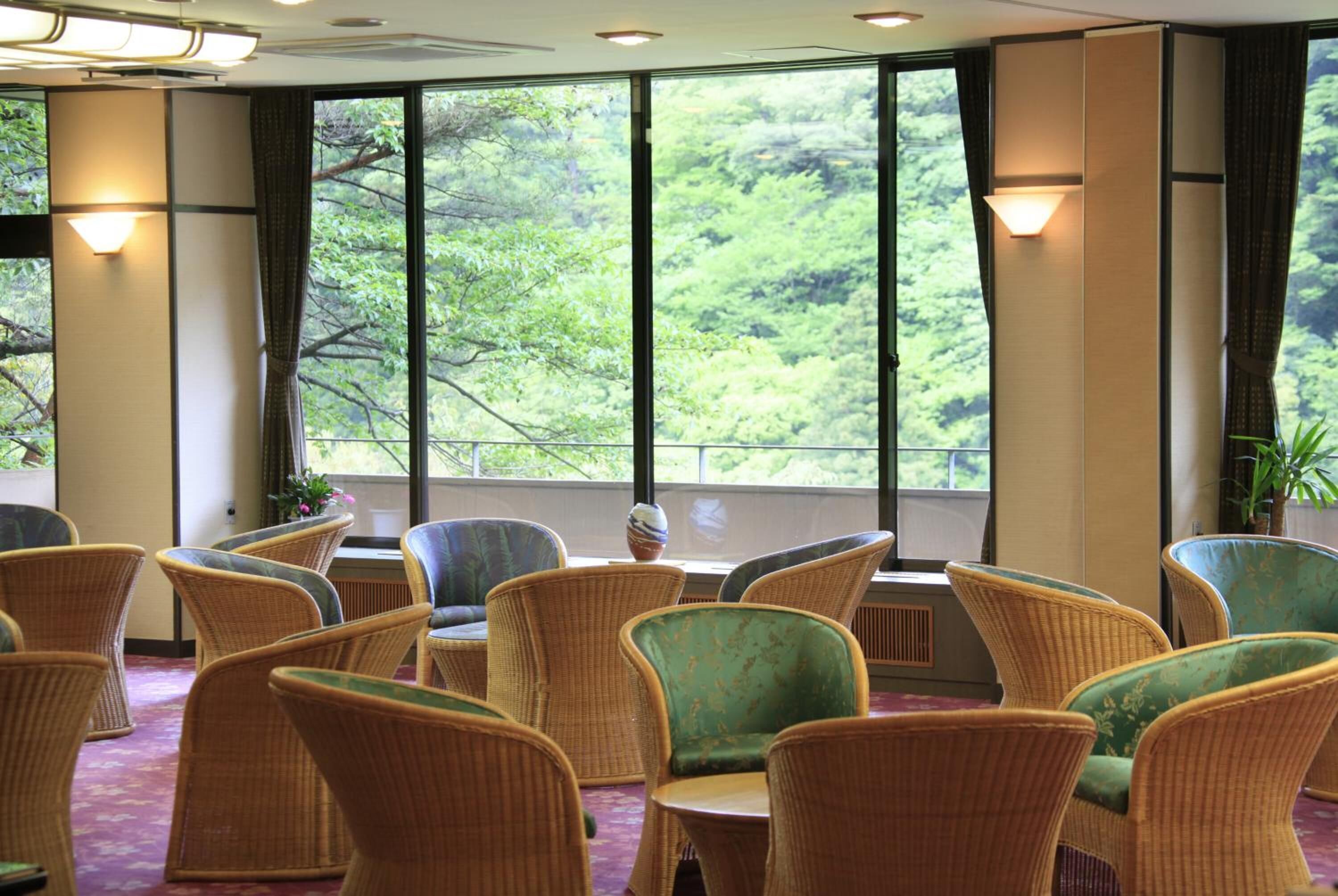 A room with wicker chairs and a view of greenery through large windows.