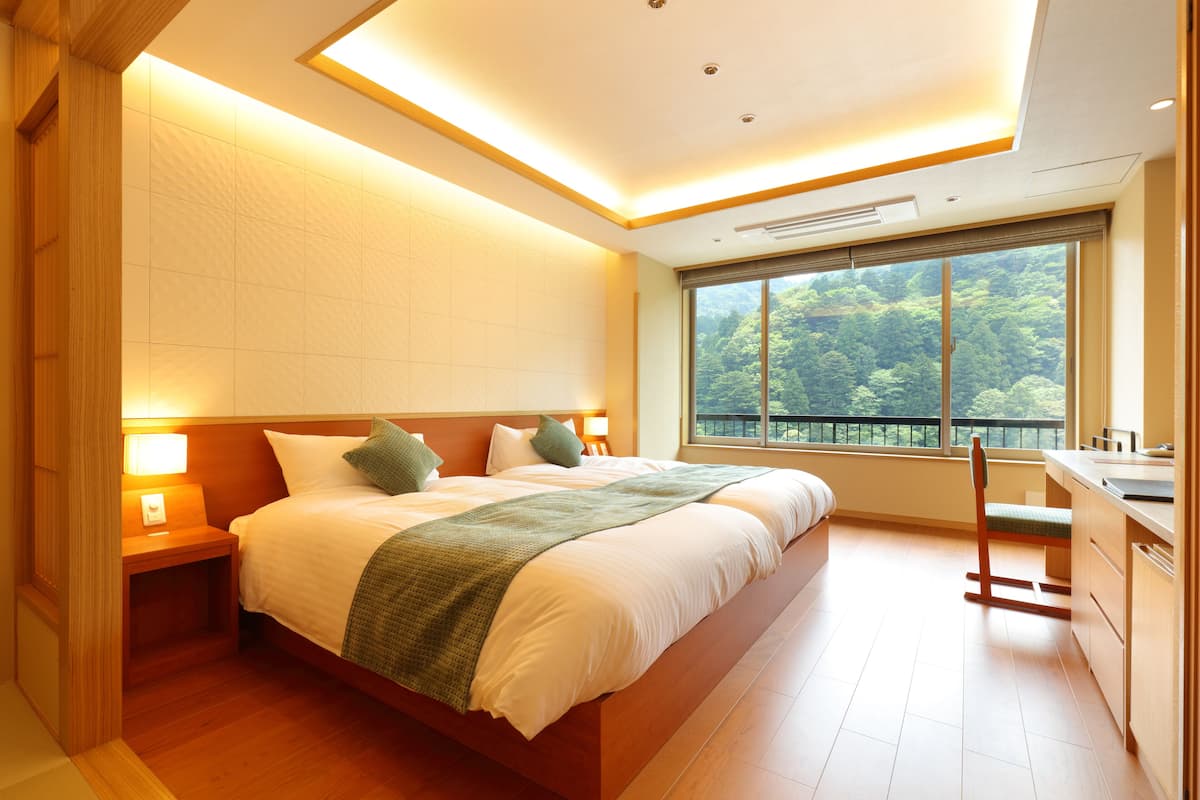 Une chambre moderne avec un grand lit, des lampes de chevet, une vue sur la verdure par la fenêtre et un espace bureau en bois.