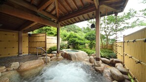 A hot spring area with a wooden roof, stone steps, and a bamboo fence.