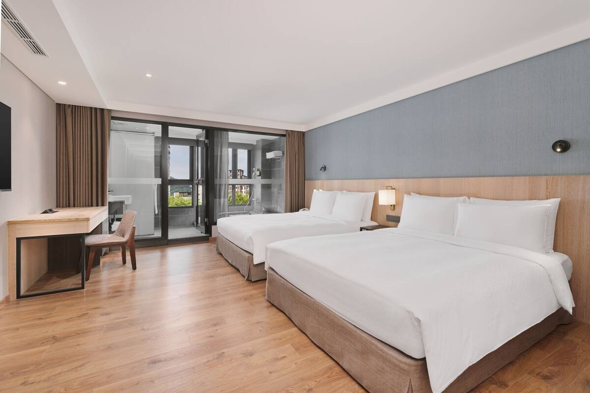 Quarto de hotel com duas camas, uma mesa e uma cadeira.