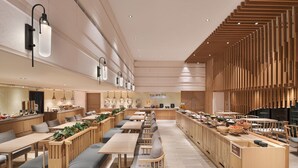 Moderni ravintola, jossa on pitkiä yhteiskäyttöisiä pöytiä, puisia penkkejä ja keskeisellä paikalla sijaitseva tiski, jossa on esillä tarjolla olevat ruoat.