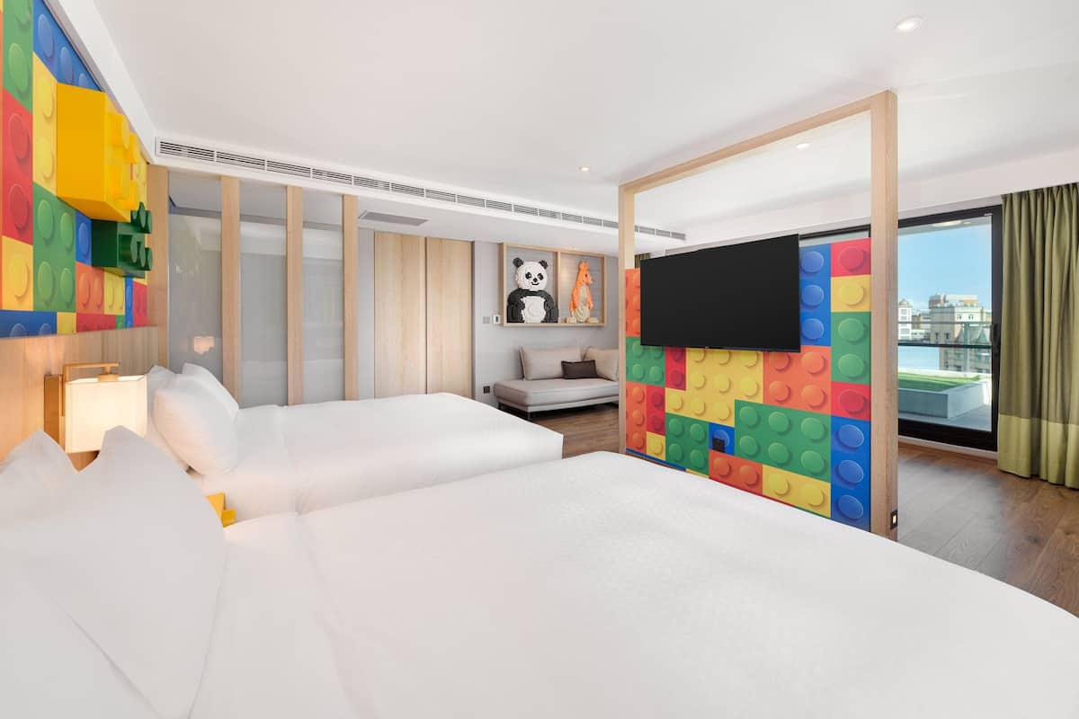 Quarto de hotel com duas camas, televisão, estátua de panda e parede colorida.
