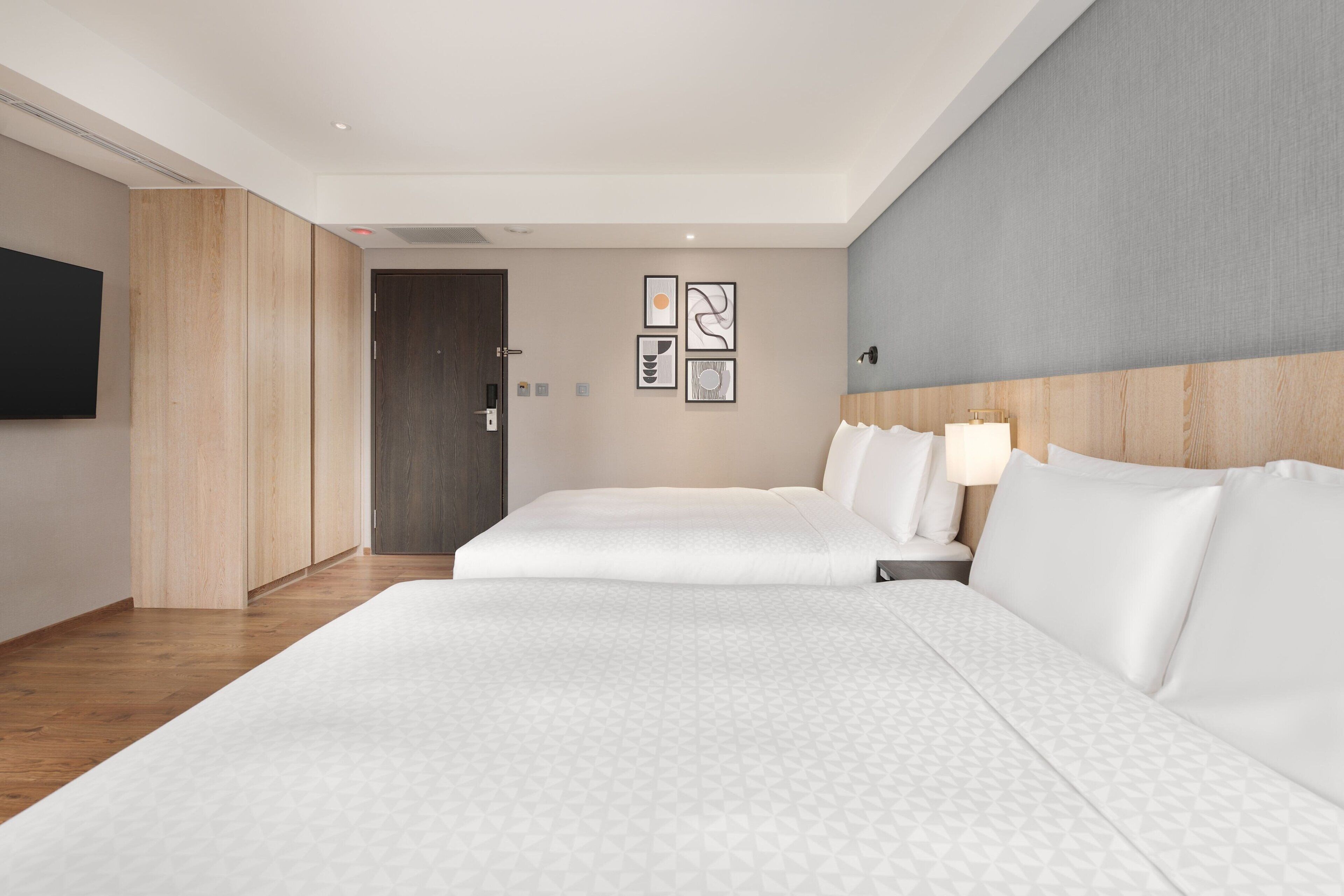 A hotel room with two beds, a wooden wardrobe, a flat-screen TV, and artwork on the wall.
