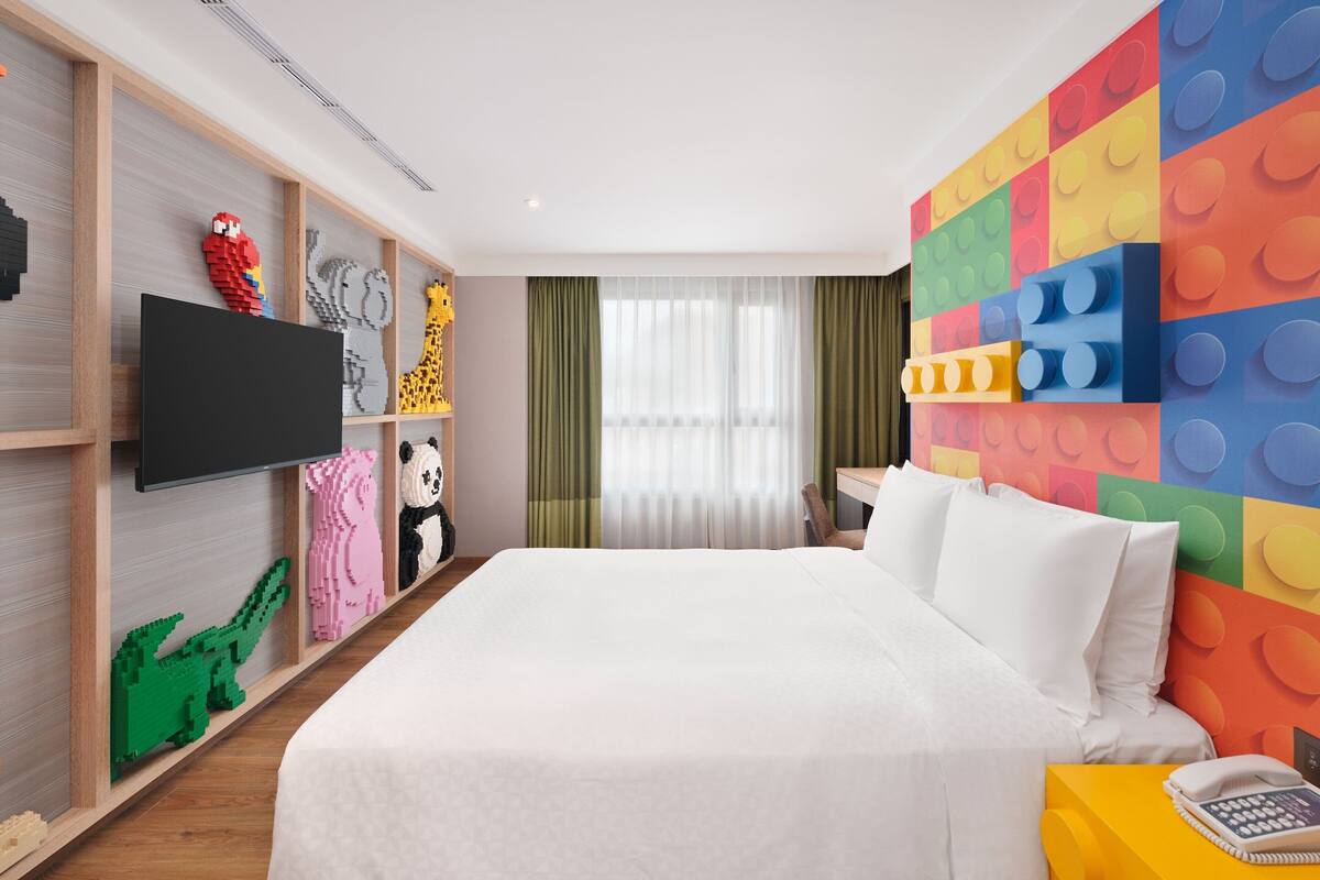 Quarto de hotel com cama, televisão, parede colorida e janela com cortinas.
