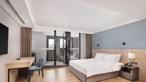 Hotellihuone, jossa on sänky, työpöytä, tuoli ja lasiovesta avautuva näkymä.