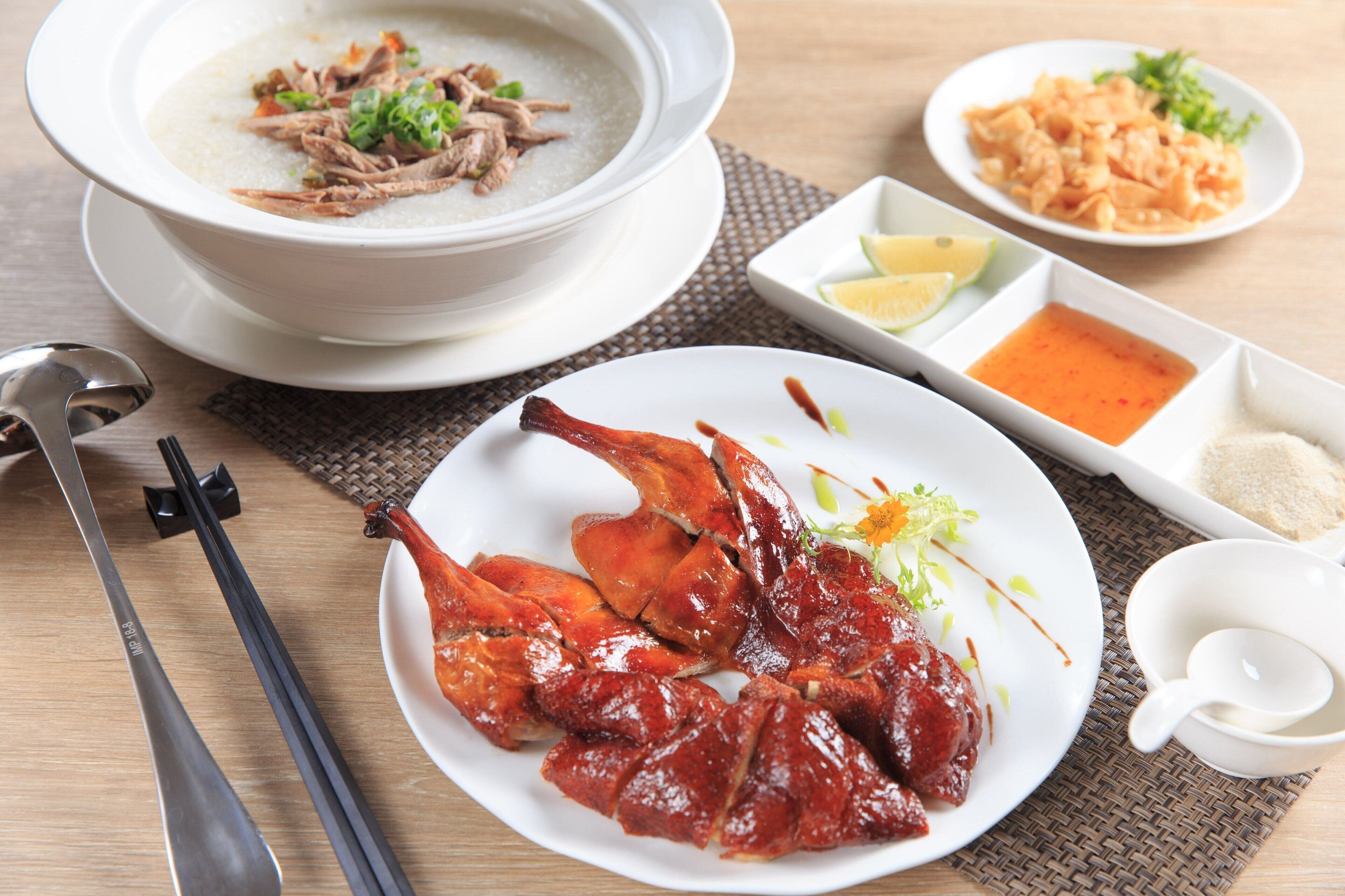A table with a bowl of soup, a plate of roasted chicken, and a plate of stir-fried vegetables.