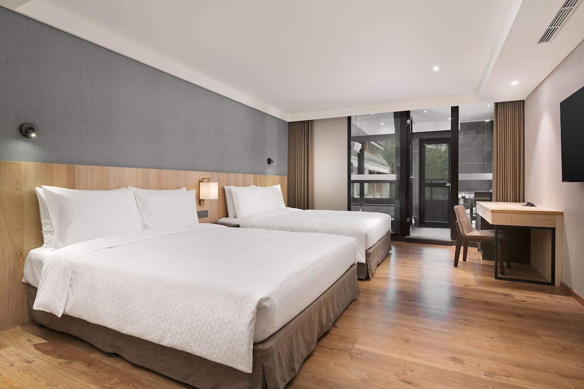 Quarto de hotel com duas camas, uma escrivaninha e vista para o exterior.