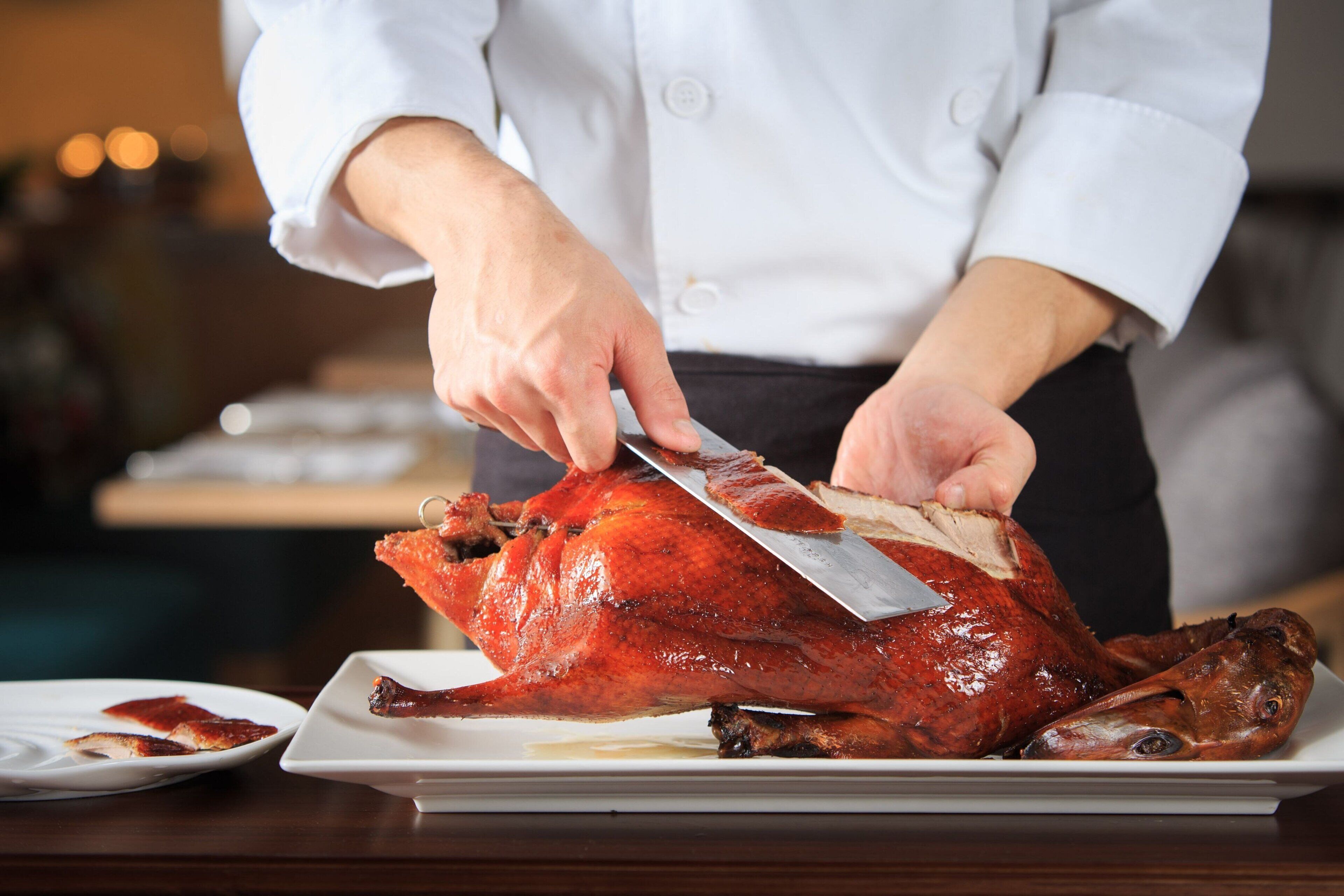 A chef carving a roasted bird on a white plate.
