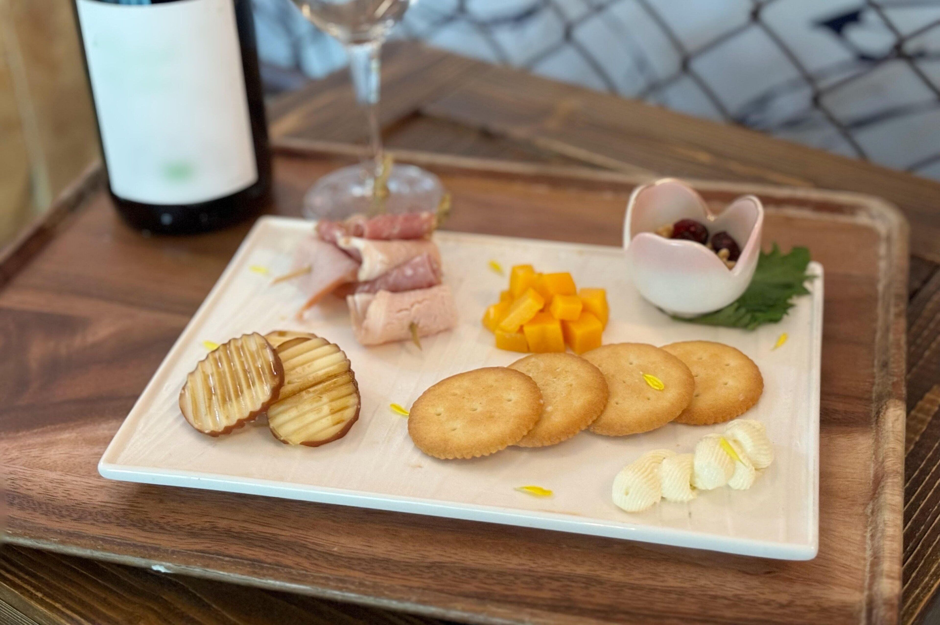 A rectangular plate with sliced meats, cheese, crackers, and a small bowl of berries on a wooden table.