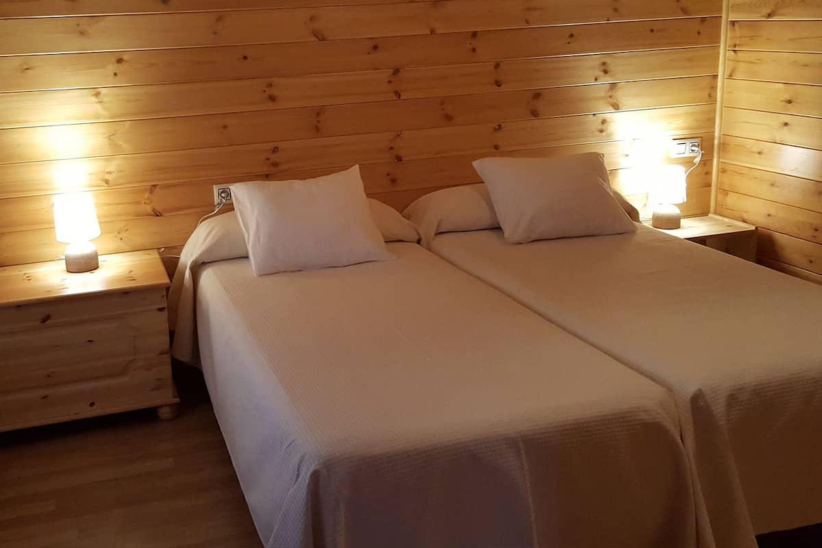 Habitación con paneles de madera, dos camas con ropa blanca y almohadas, y dos lámparas de noche.