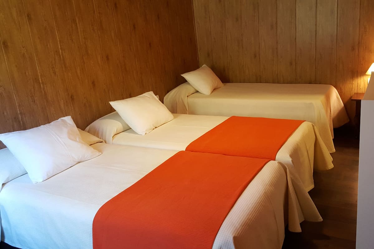 Habitación de hotel con dos camas, cada una con ropa blanca y almohadones naranjas.