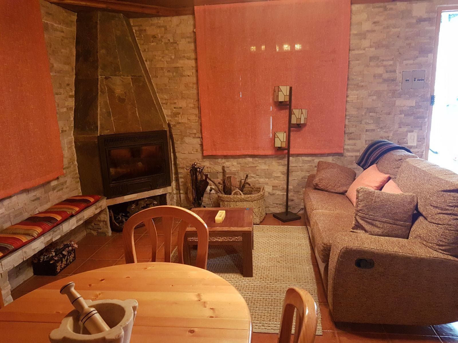 Un salon chaleureux avec une cheminée, un canapé, une table à manger avec une chaise et un lampadaire.