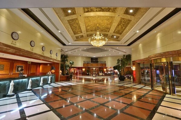 A spacious lobby with a marble floor, a grand chandelier, and a reception desk with a counter. - Qingdao Huiquan Dynasty Hotel (QINGDAO)