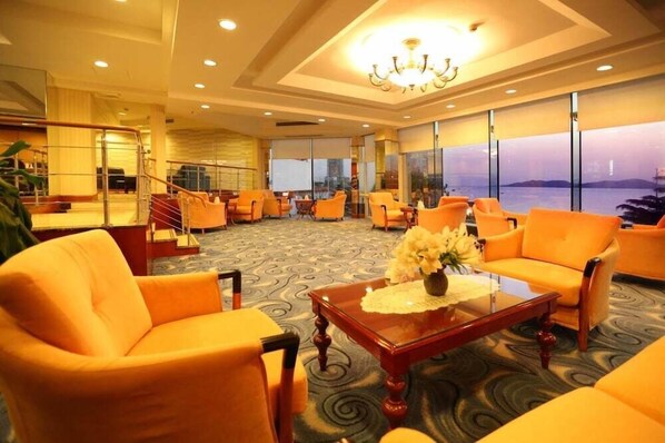 A hotel lobby with orange seating, a chandelier, and large windows overlooking a body of water. - Qingdao Huiquan Dynasty Hotel (QINGDAO)