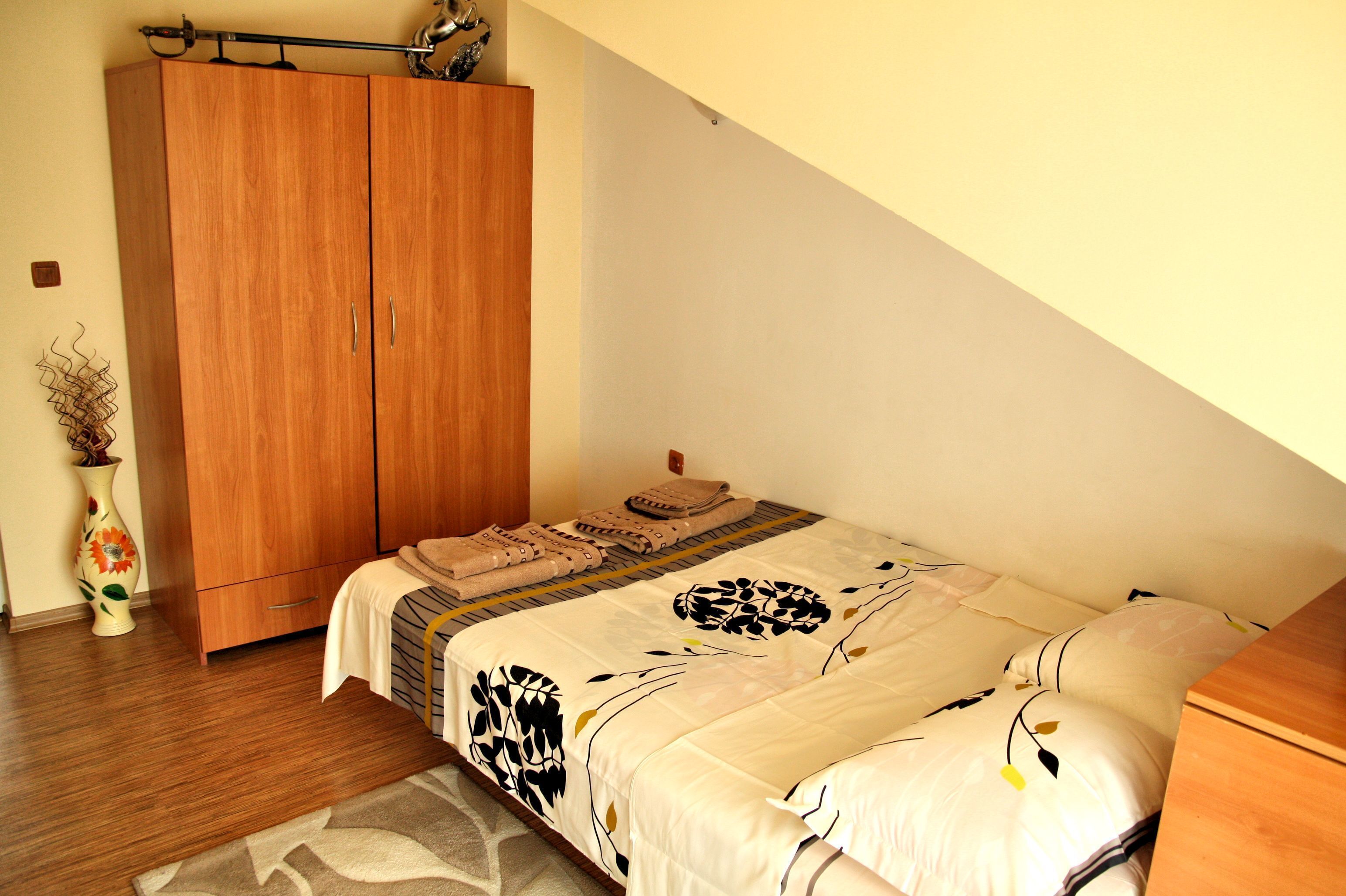 A bedroom with a bed, wooden wardrobe, and a vase with flowers.