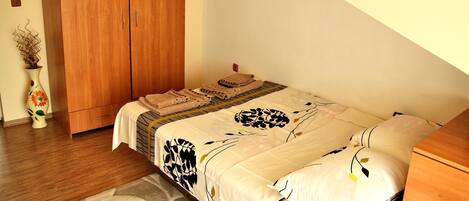 A bedroom with a bed, wooden wardrobe, and a vase with flowers.