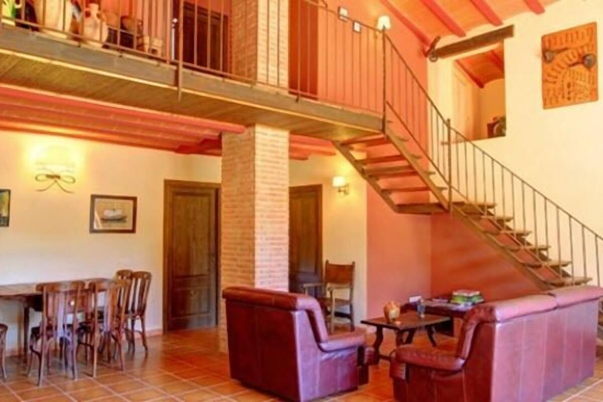 A spacious living area with a high ceiling, a staircase, and a dining area with wooden furniture.