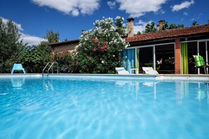 A swimming pool with lounge chairs and a slide, surrounded by lush greenery and a house with large windows. - La Villa des Violettes (Toulouse)