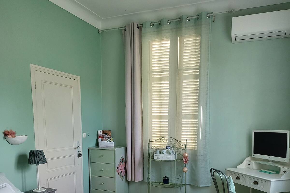 Un dormitorio con cama, escritorio, silla, armario y ventana con cortinas.