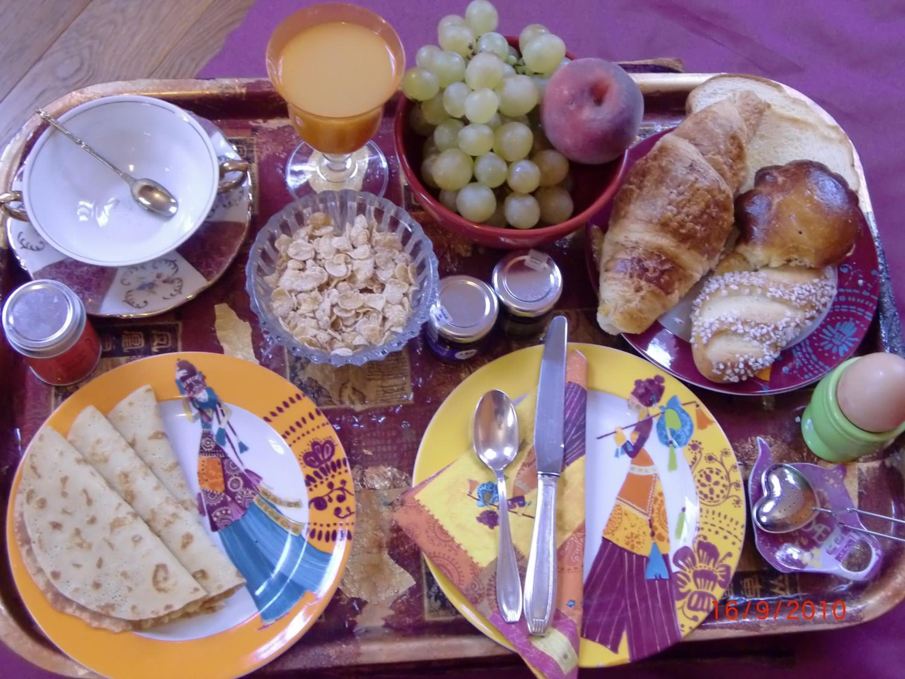 Ett frukostbricka med olika sorters mat och dryck, inklusive croissanter, vindruvor och ett glas apelsinjuice.
