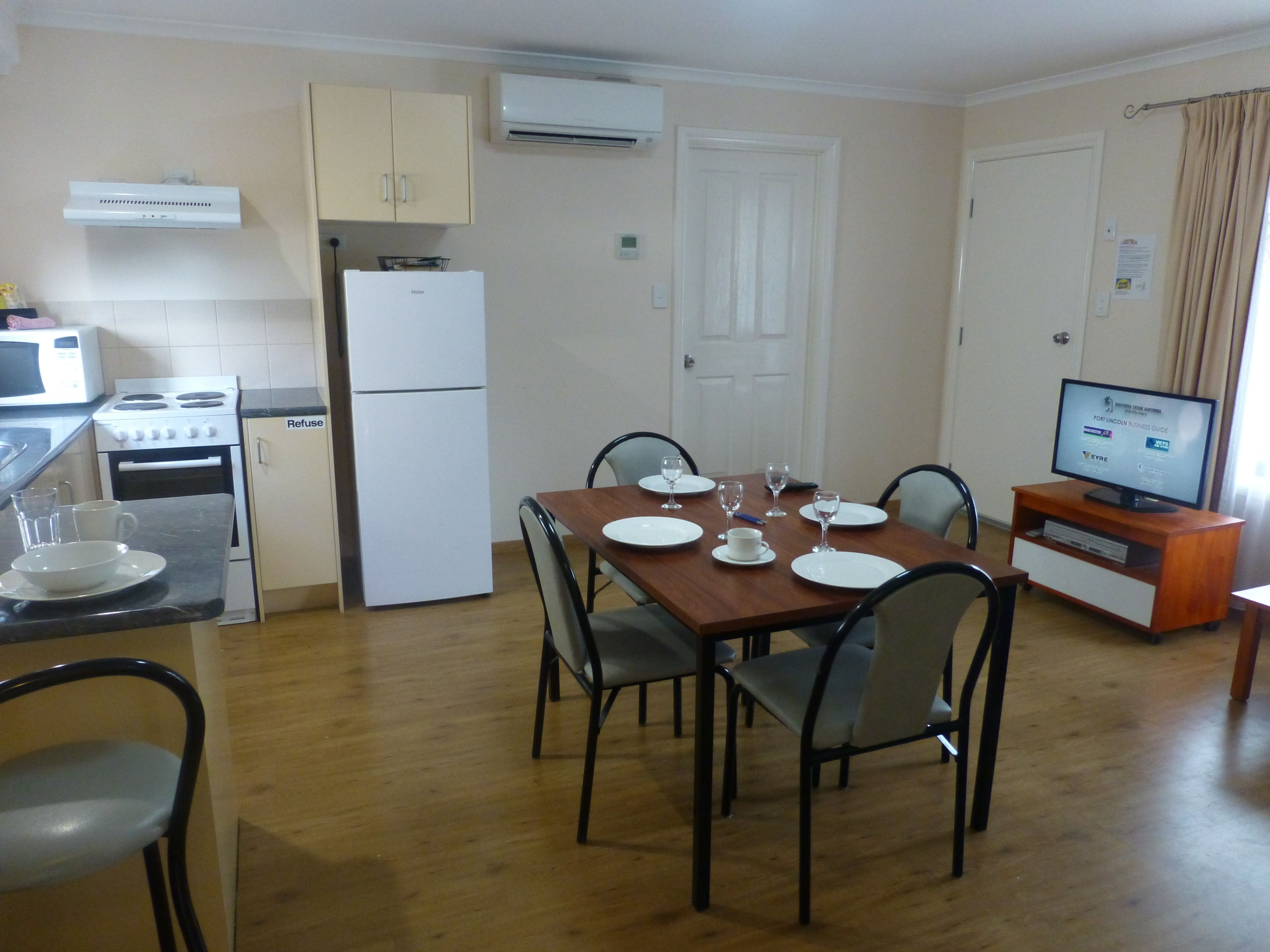 Una cocina funcional con estufa, microondas y refrigerador. Hay una mesa de comedor con platos, vasos y un televisor sobre un mueble.