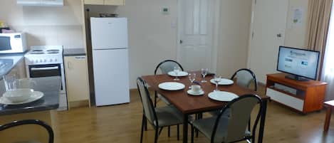 Una cocina funcional con estufa, microondas y refrigerador. Hay una mesa de comedor con platos, vasos y un televisor sobre un mueble.