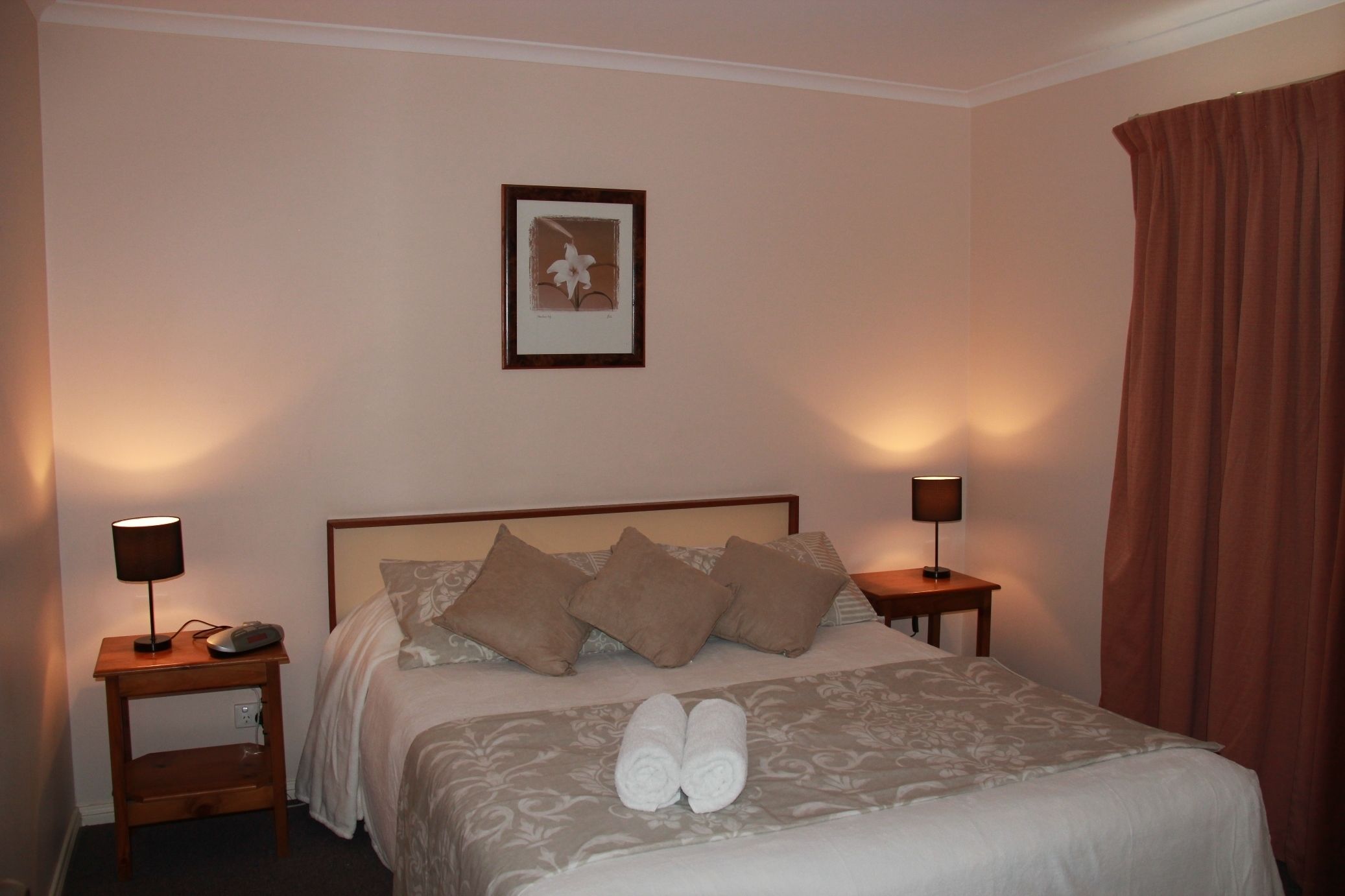 A neatly made bed with a headboard, two bedside tables with lamps, and a framed picture on the wall.