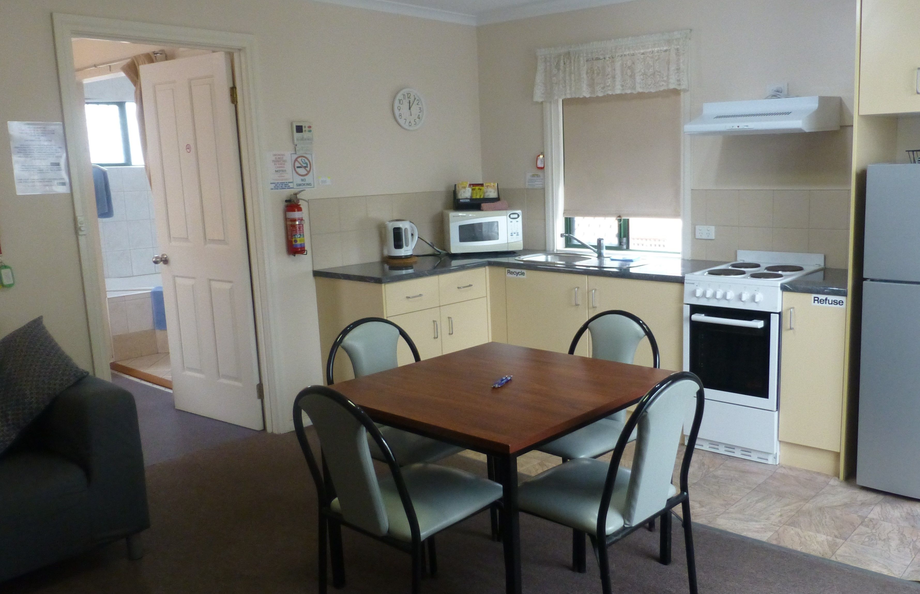 A compact kitchen with a microwave, stove, and refrigerator. There is a dining table with four chairs.