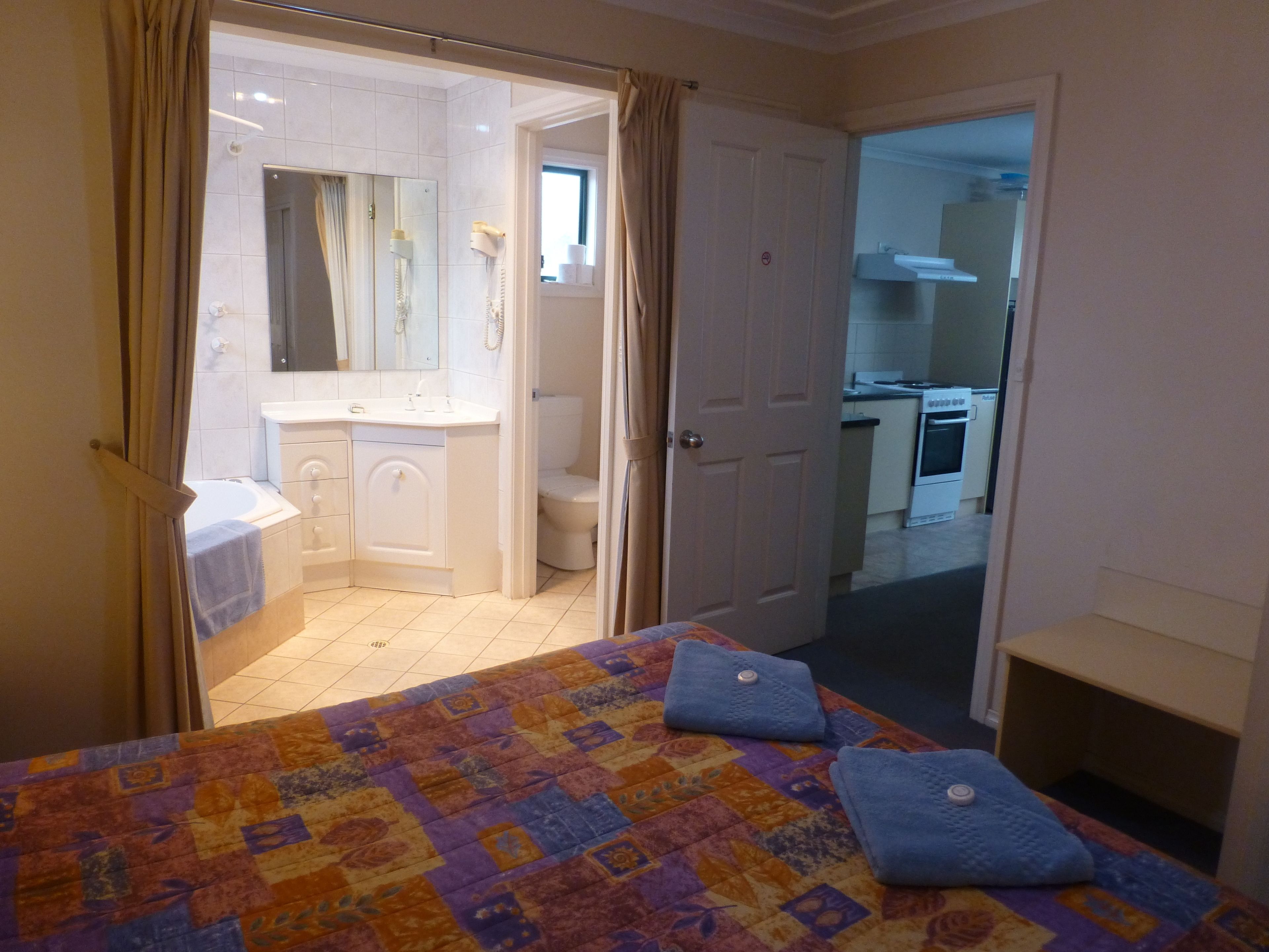 A bedroom with a bed, a bathroom with a sink and toilet, and a kitchen visible through an open door.
