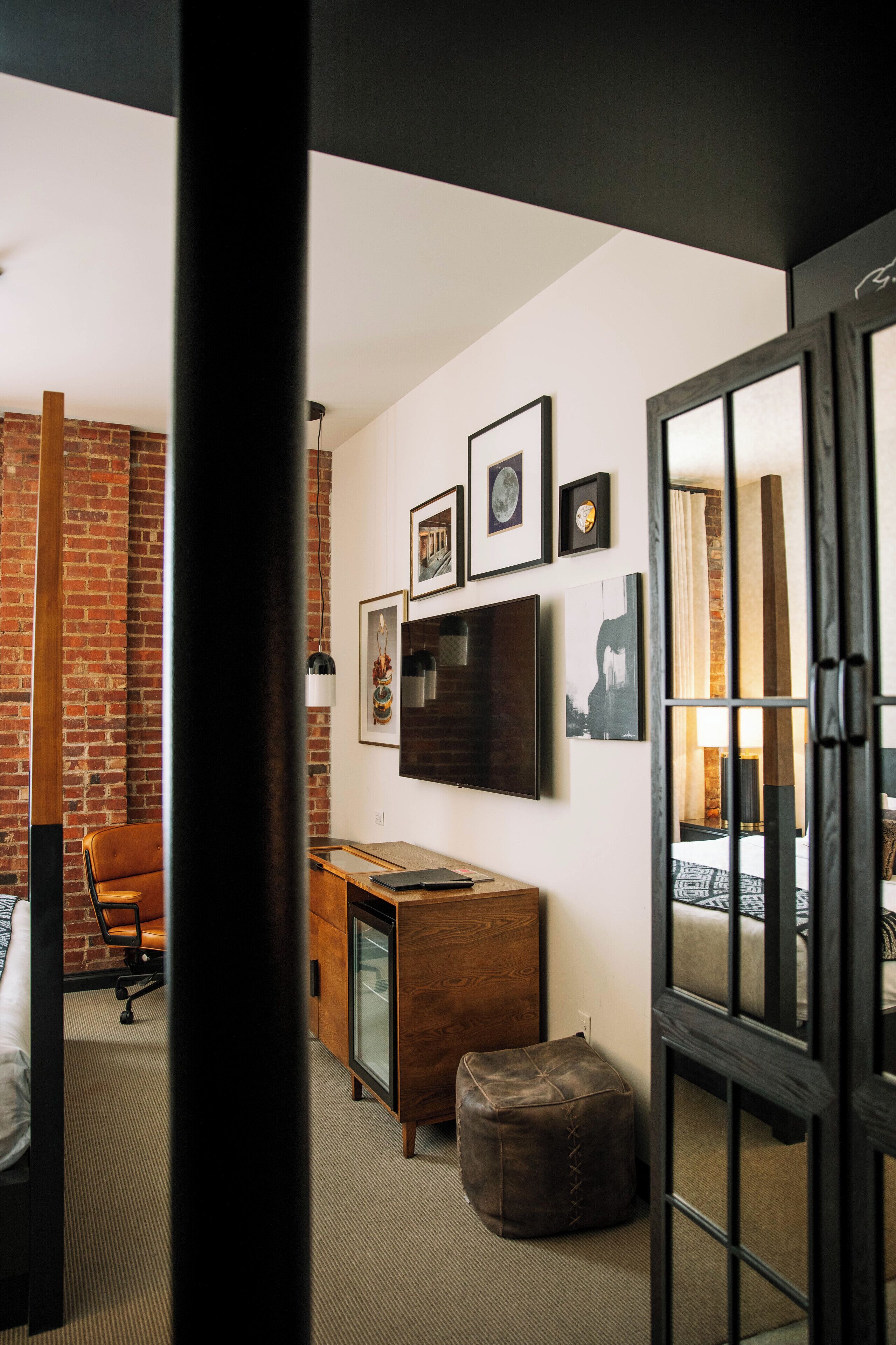 A hotel room with a brick wall, a desk with a computer, a bed, and a large mirror.