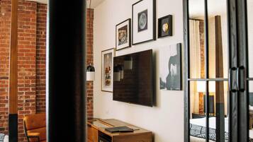 A hotel room with a brick wall, a desk with a computer, a bed, and a large mirror.