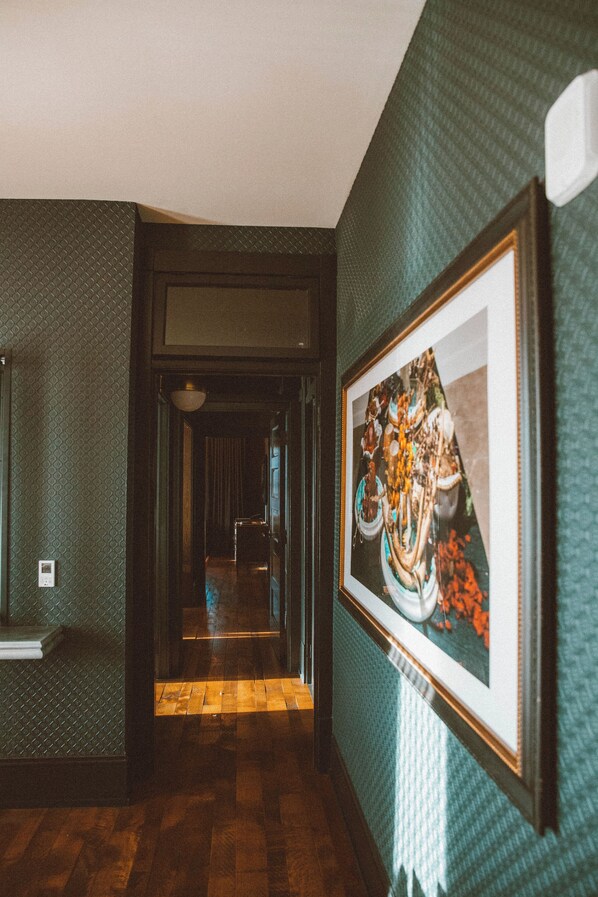 A hallway with patterned walls, a framed artwork, and wooden flooring. - Crossroads Hotel (Kansas City)