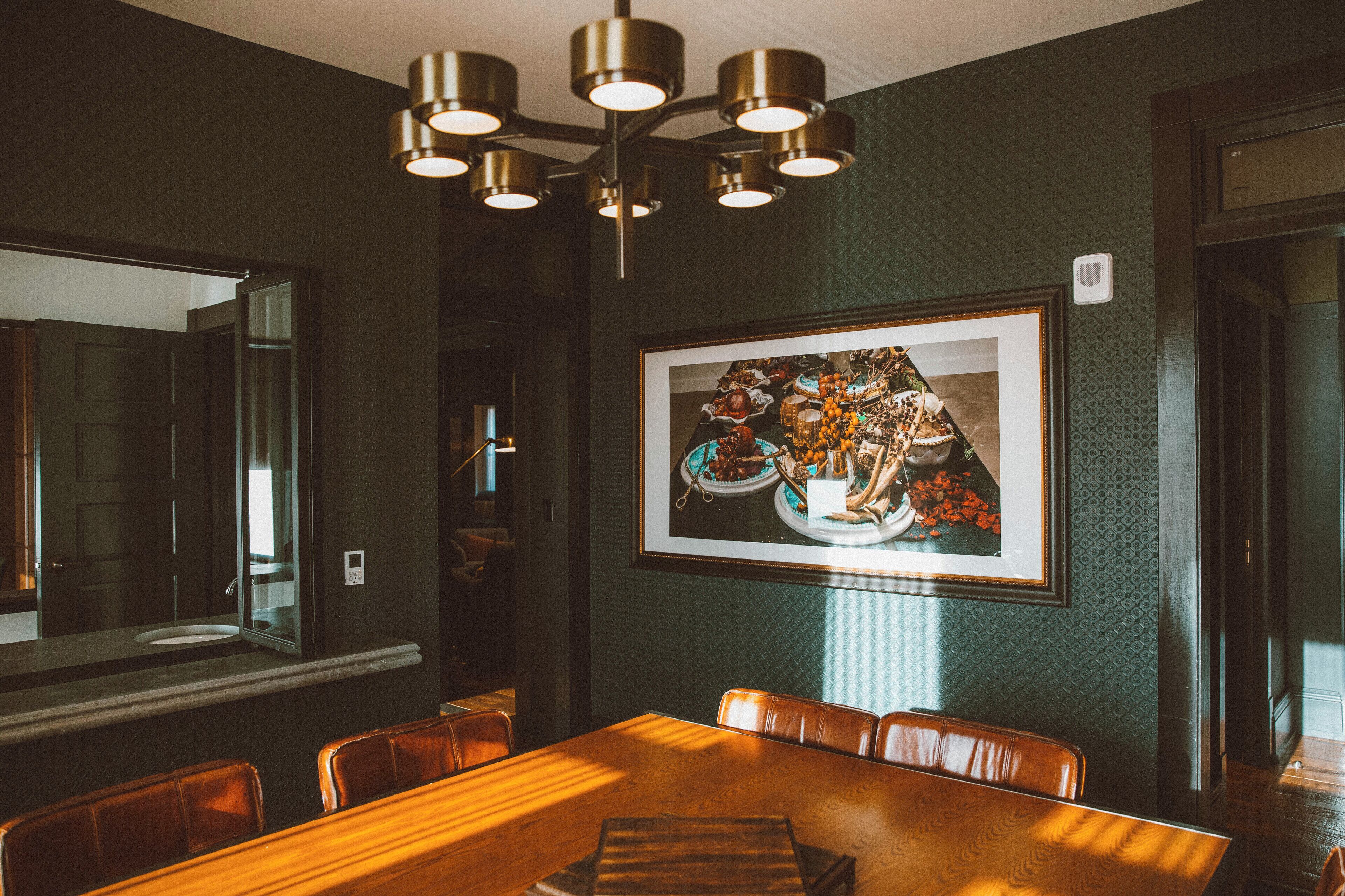 A dining area with a wooden table, leather chairs, a framed picture on the wall, and a ceiling light fixture.
