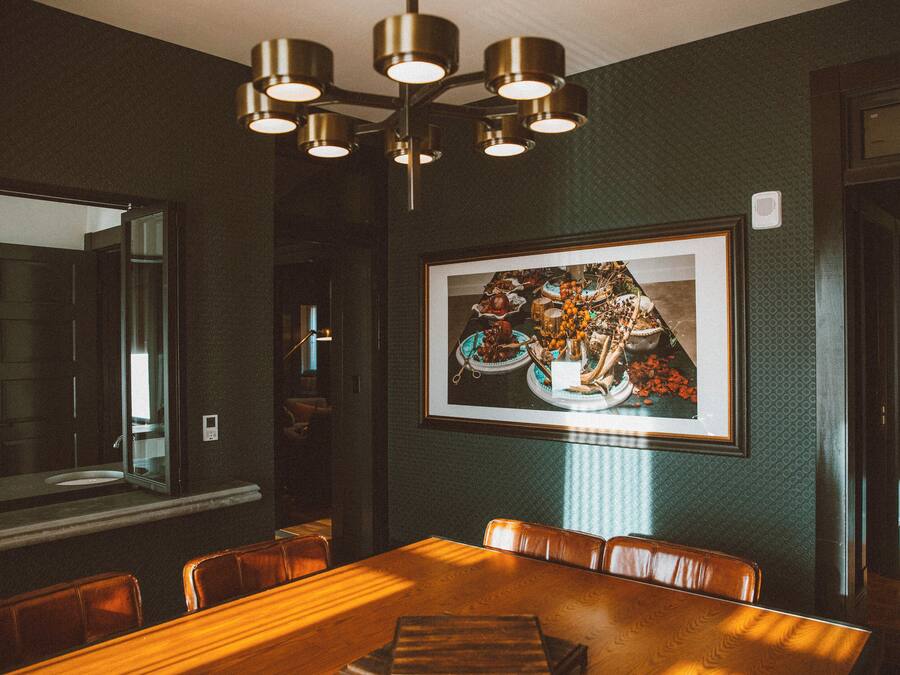 A dining area with a wooden table, leather chairs, a framed picture on the wall, and a ceiling light fixture.