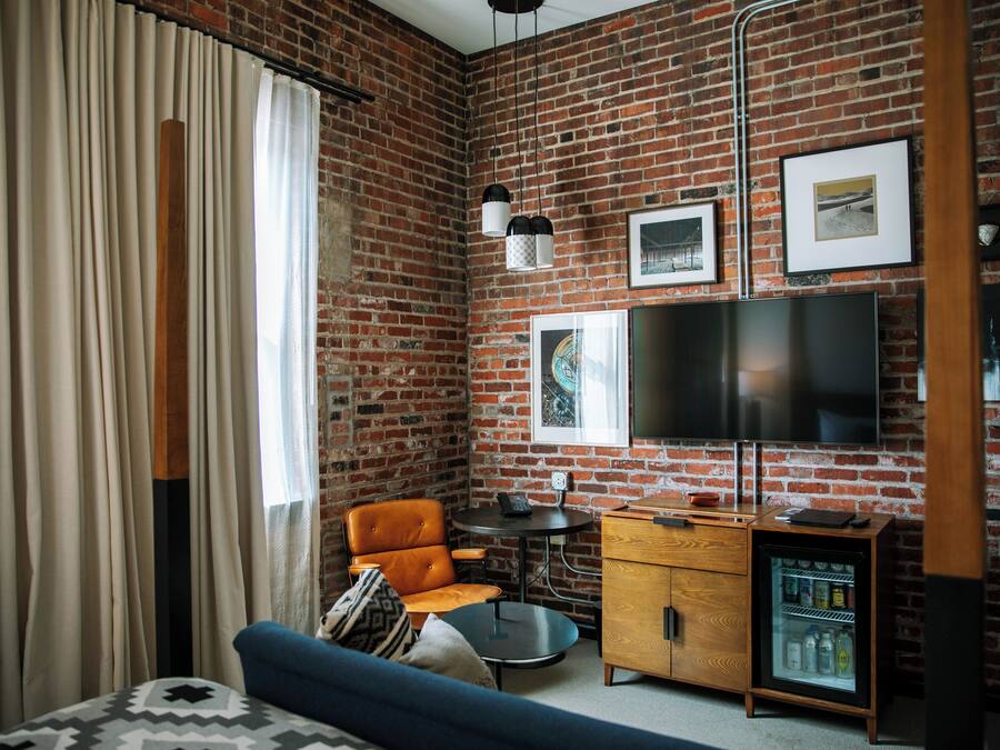Ein Zimmer mit Backsteinwand, einer Couch, einem Sessel, einem kleinen Tisch, einem Fernseher und einem Minikühlschrank.
