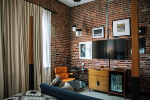 Una habitación con pared de ladrillo, sofá, sillón, una mesita, televisor y refrigerador pequeño.