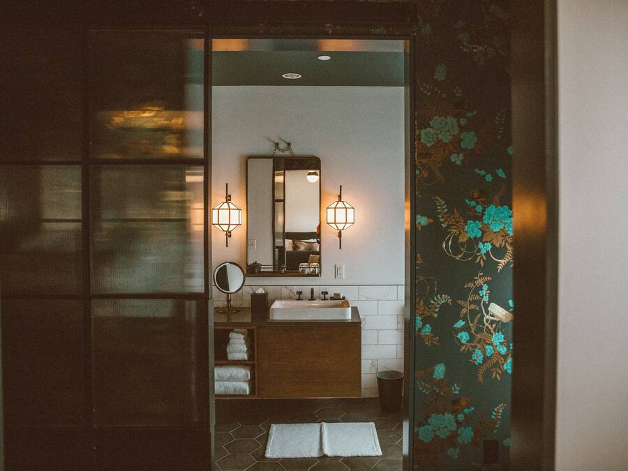 A bathroom with a wooden vanity, a mirror, two wall-mounted lights, and a tiled floor.