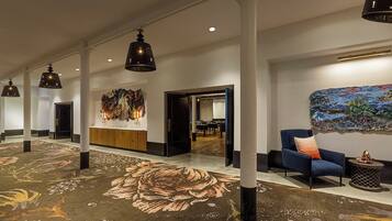 A spacious lobby with a floral carpet, modern lighting, a reception desk, and a colorful abstract painting.
