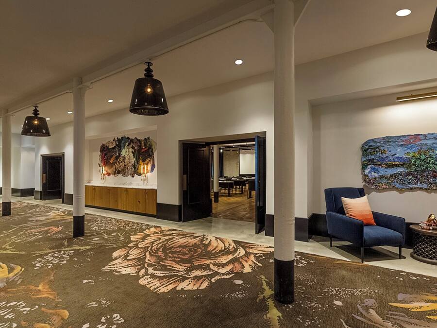 A spacious lobby with a floral carpet, modern lighting, a reception desk, and a colorful abstract painting.